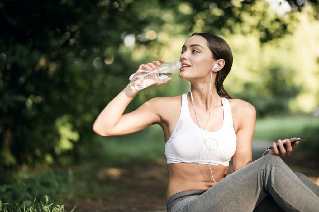 Жена пие вода от бутилка по време на тренировка.