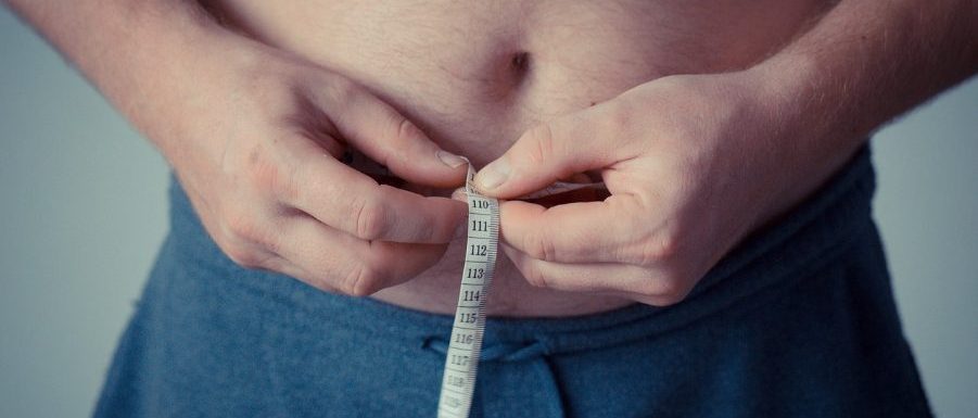 Мъж в спортно облекло измерва талията си със сантиметър.