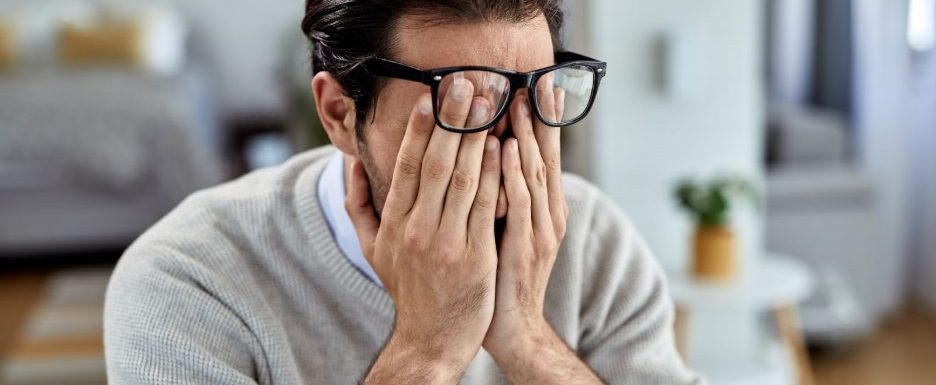 Мъж с очила, който прикрива очите си с ръце и изглежда стресиран